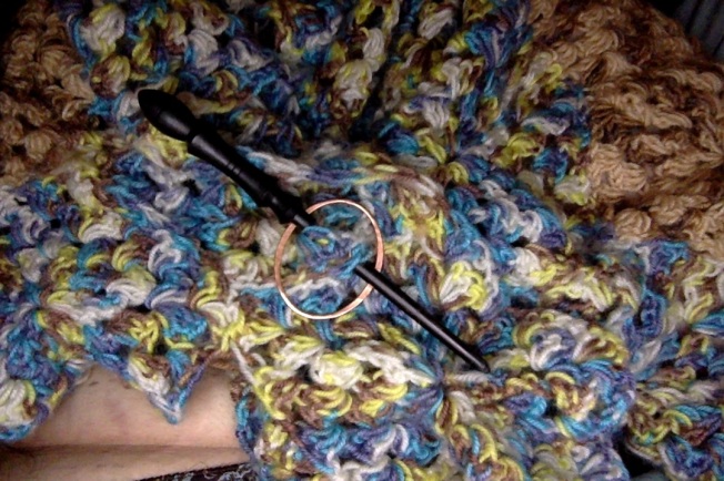 Closeup of a crocheted afghan worn as a shawl, with a shawl pin.