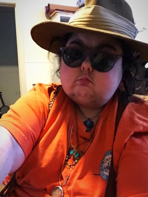 Mel wearing an orange shirt, dark glasses, and a brown Aussie hat.